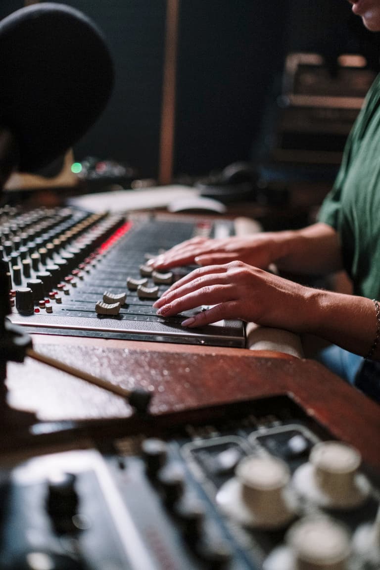an image of someone sitting at a mixing desk, hands on the console